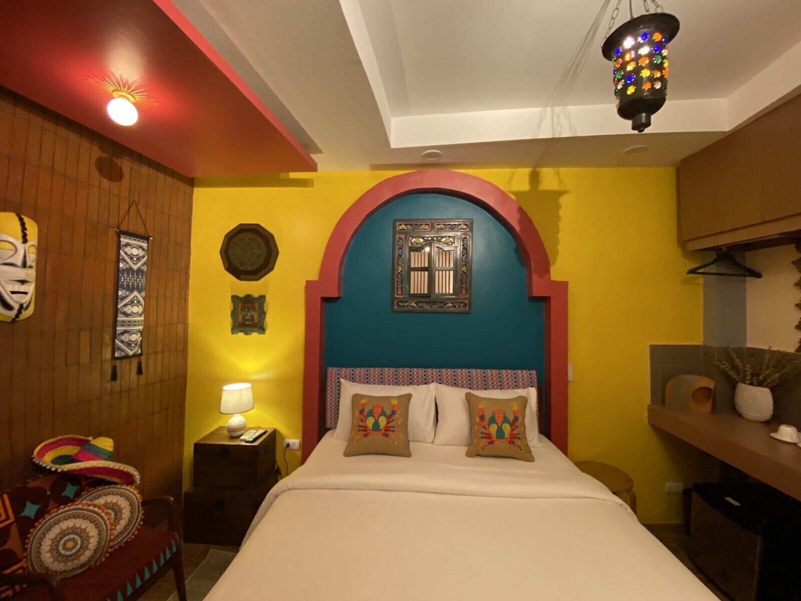 Una stanza arredata con un letto, un comodino, una lampada, una parete decorata e un lampadario.