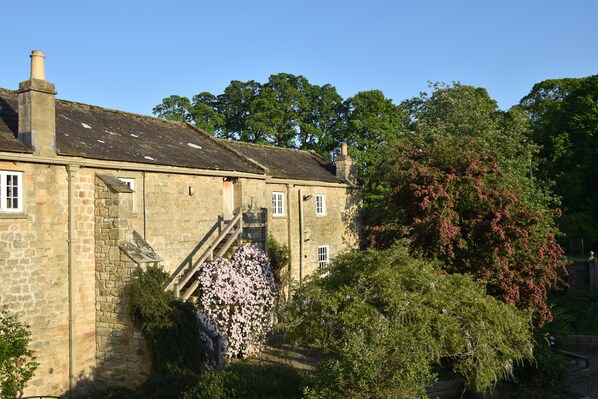A stone building with a staircase leading to a door, surrounded by greenery and trees. - The Coach House at Jervaulx (Ripon)