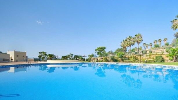 A clear blue swimming pool with a tiled edge, surrounded by palm trees and a building with a flat roof. - 16Benalmádena Cibeles, Pool View, Terrace, Golf (Benalmádena)