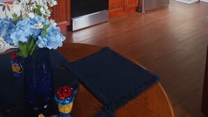 A modern kitchen with wooden cabinets, stainless steel appliances, and a blue floral centerpiece on the table.