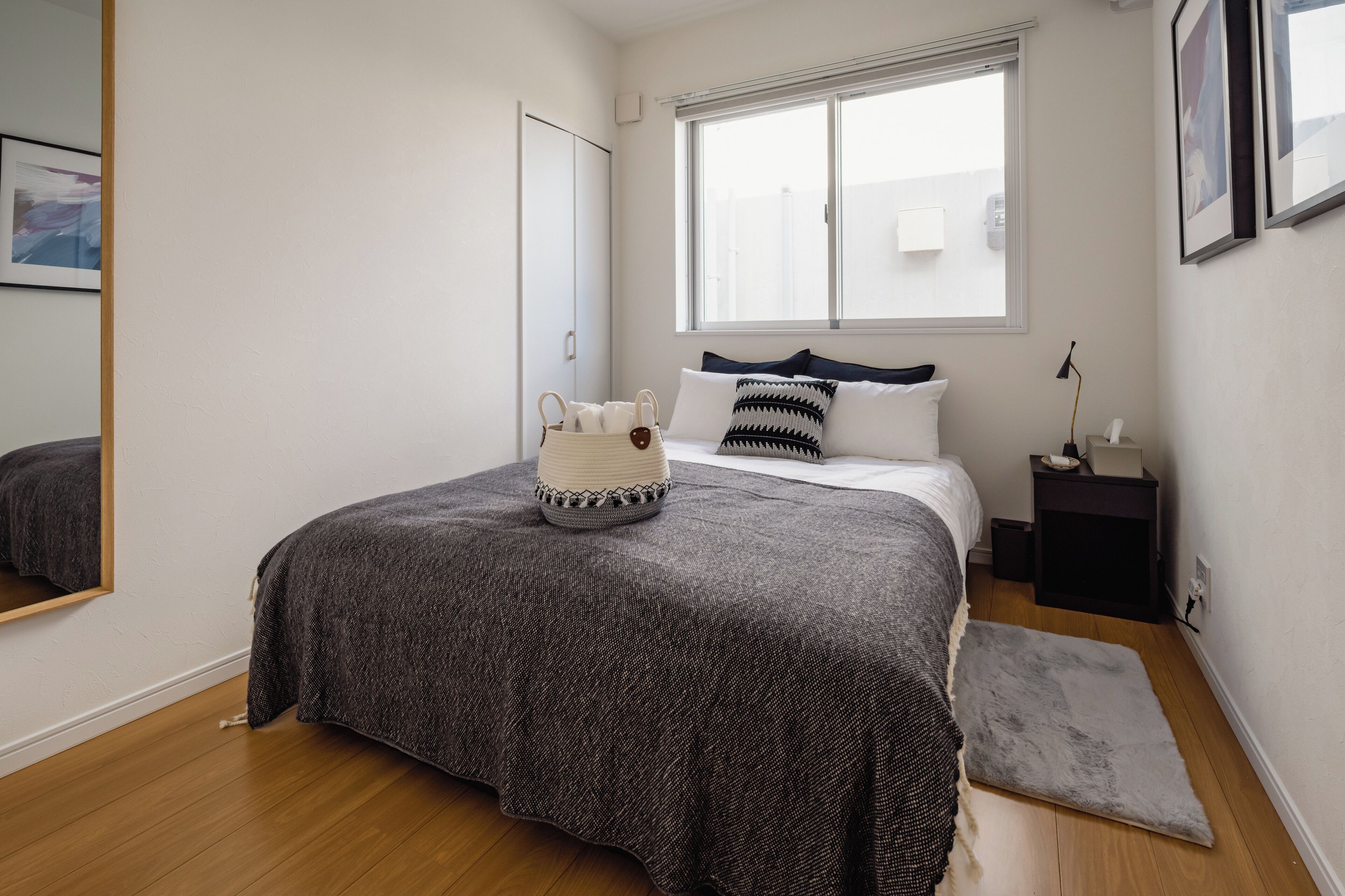 Une chambre à coucher avec un lit, une table de chevet, une lampe, une fenêtre et un miroir.