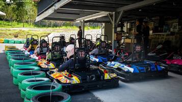 Go-karts lined up with drivers ready to race, a covered area with a roof, and a building with a sign.