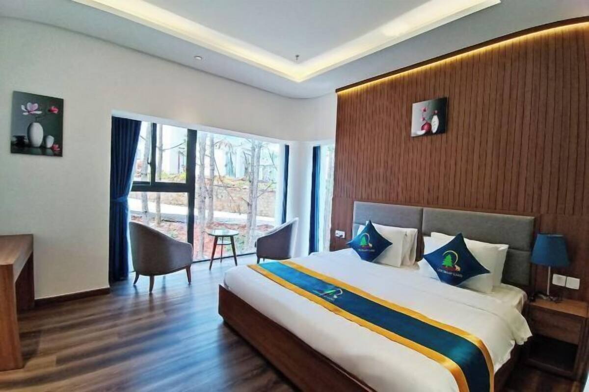 Ein modernes Hotelzimmer mit einem großen Bett, einem Holz-Kopfteil, einem Schreibtisch und Blick ins Freie.