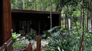 A wooden structure with a stone pathway leading to it, surrounded by lush greenery and various plants.