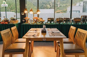 A dining area with a table set for two, wooden chairs, and a buffet with various food items. - Rung Thong Nui Voi Villa & Resort (Hiep Thanh)