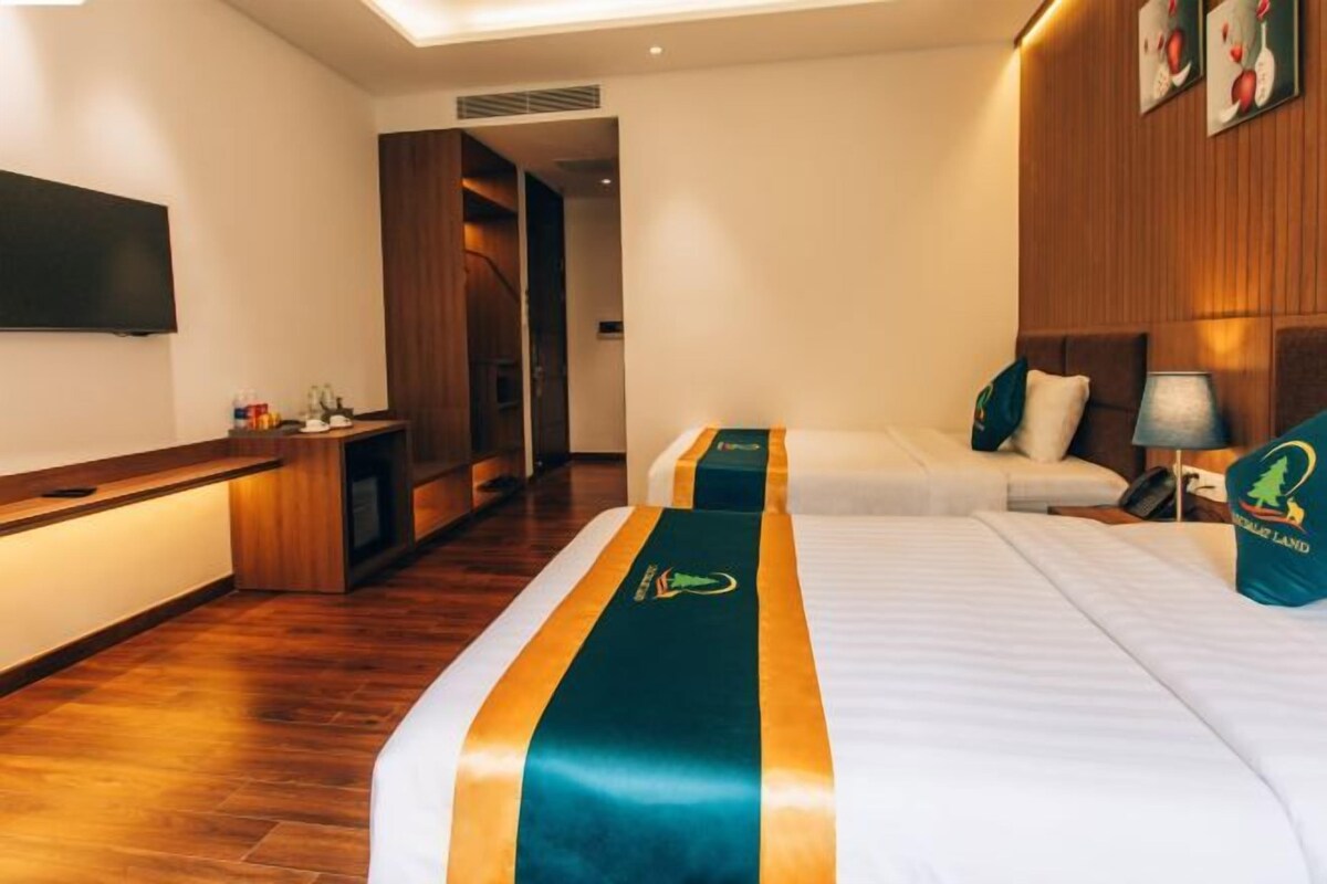 Habitación de hotel con dos camas, televisor, escritorio y piso de madera.