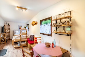 A cozy room with a wooden bed, a red and white checkered table, a shelf with glassware, and a window with a view.