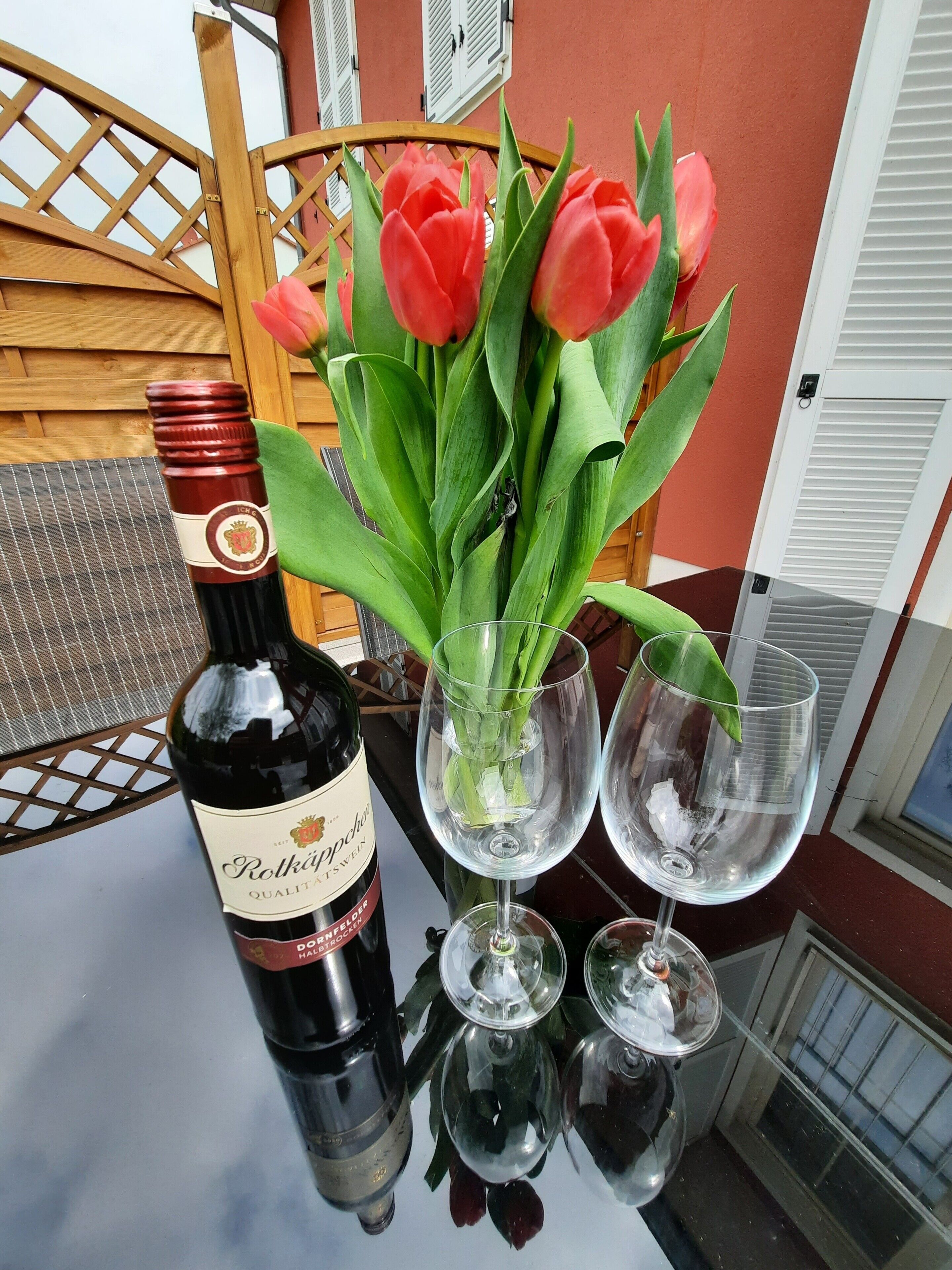 A bottle of wine, a vase with red tulips, and two empty wine glasses on a table.