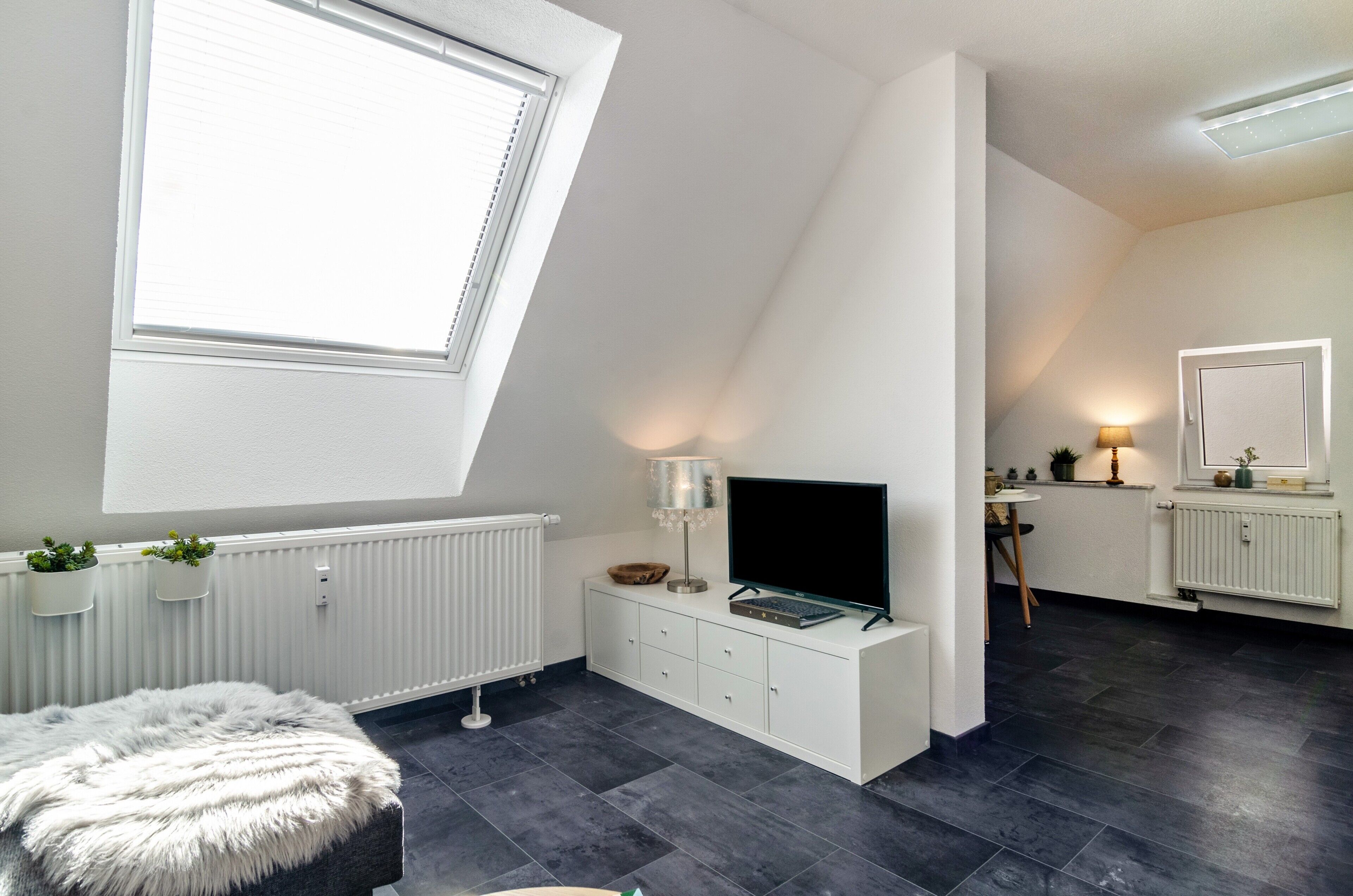 A modern bedroom with a skylight, white furniture, a flat-screen TV, and a small dining area.