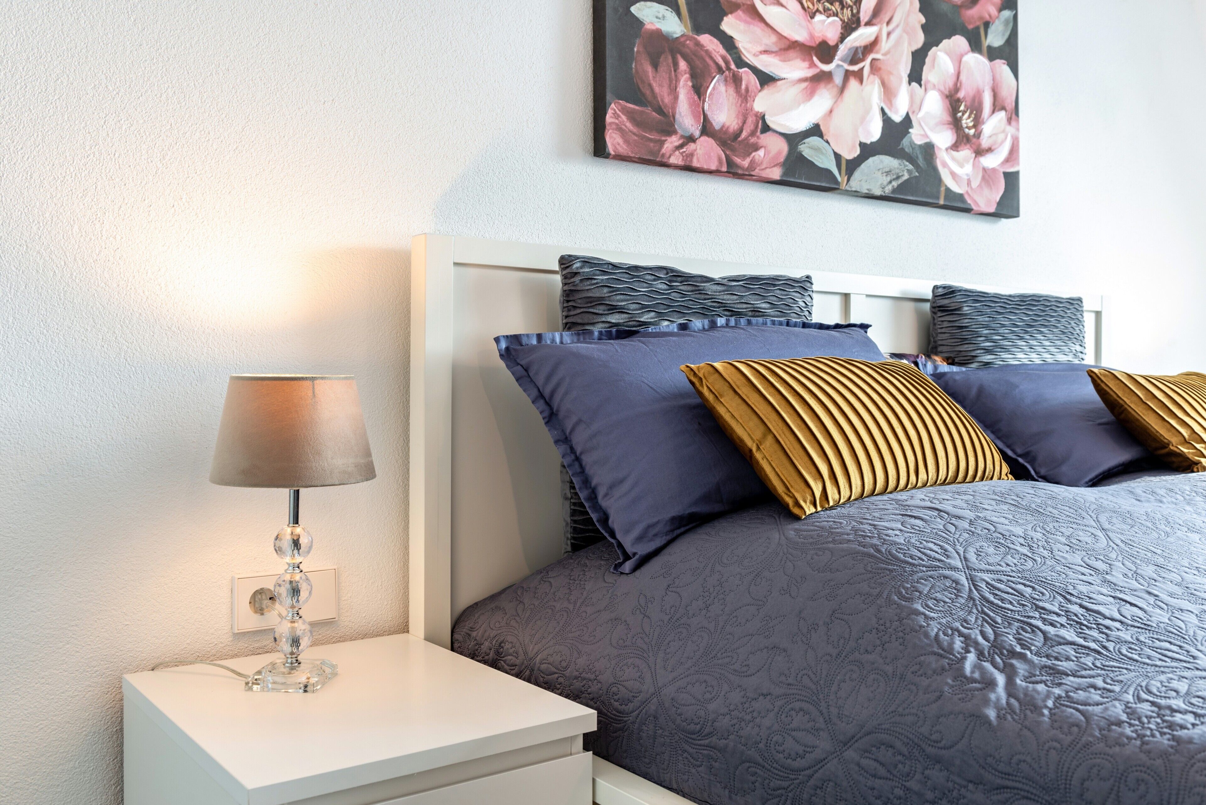A neatly arranged bedroom with a bed, pillows, a bedside table, and a lamp.