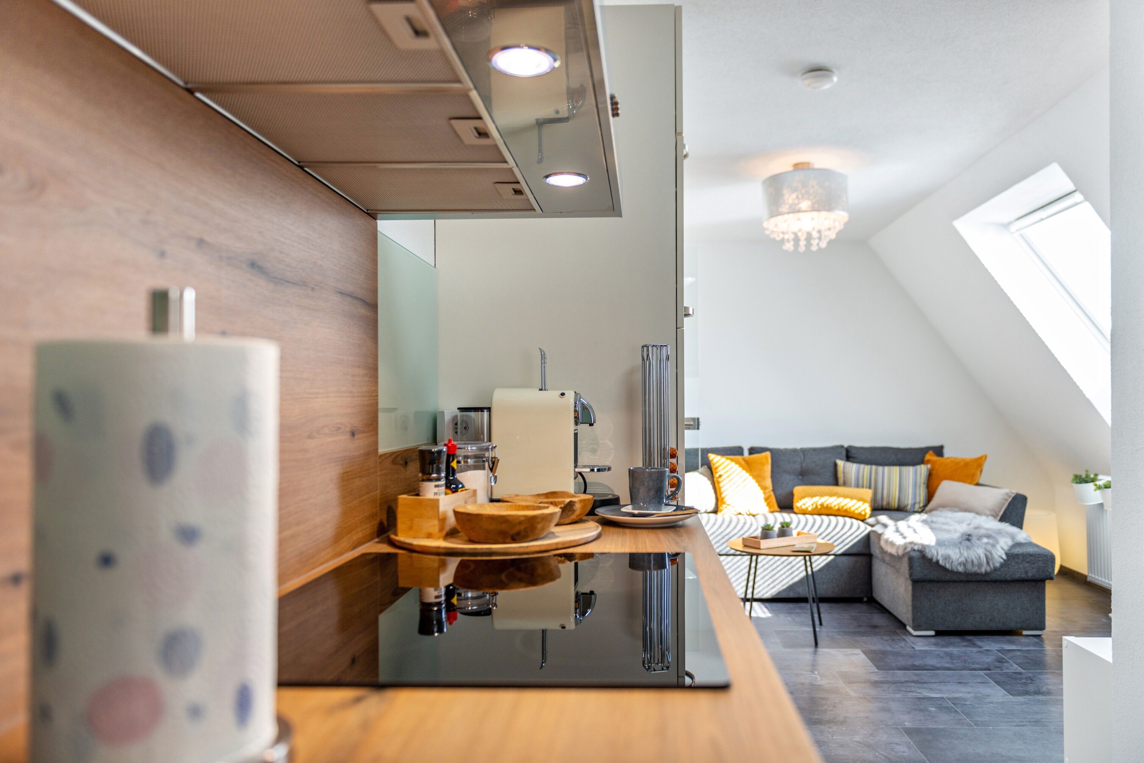 A modern kitchen with a coffee machine, a wooden countertop, and a dining area with a sofa and cushions.