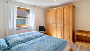 Un dormitorio con dos camas, un armario de madera, una silla y una ventana con cortinas.