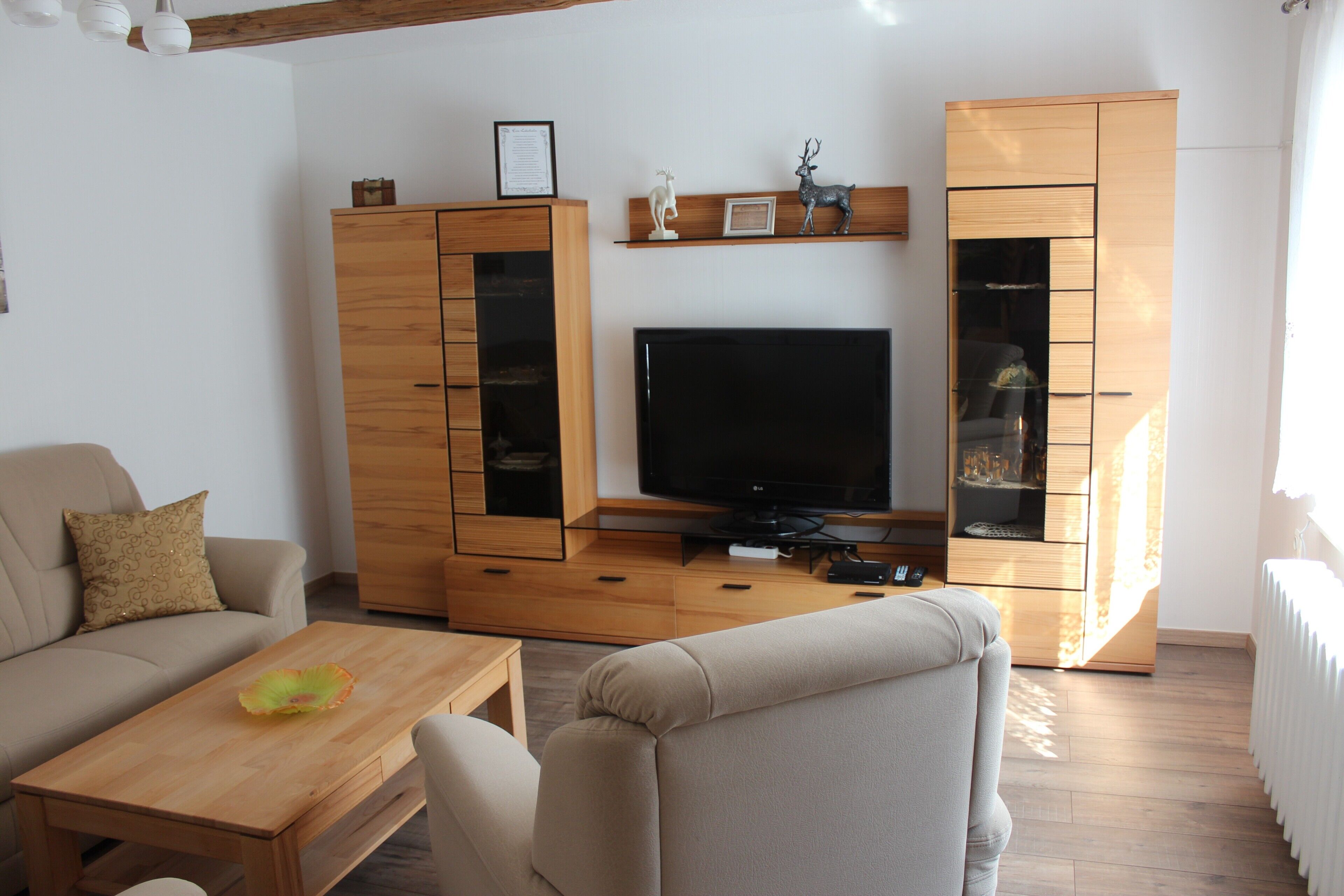 Una sala de estar con un sofá, una mesa de centro, un televisor, armarios de madera y un estante con objetos decorativos.