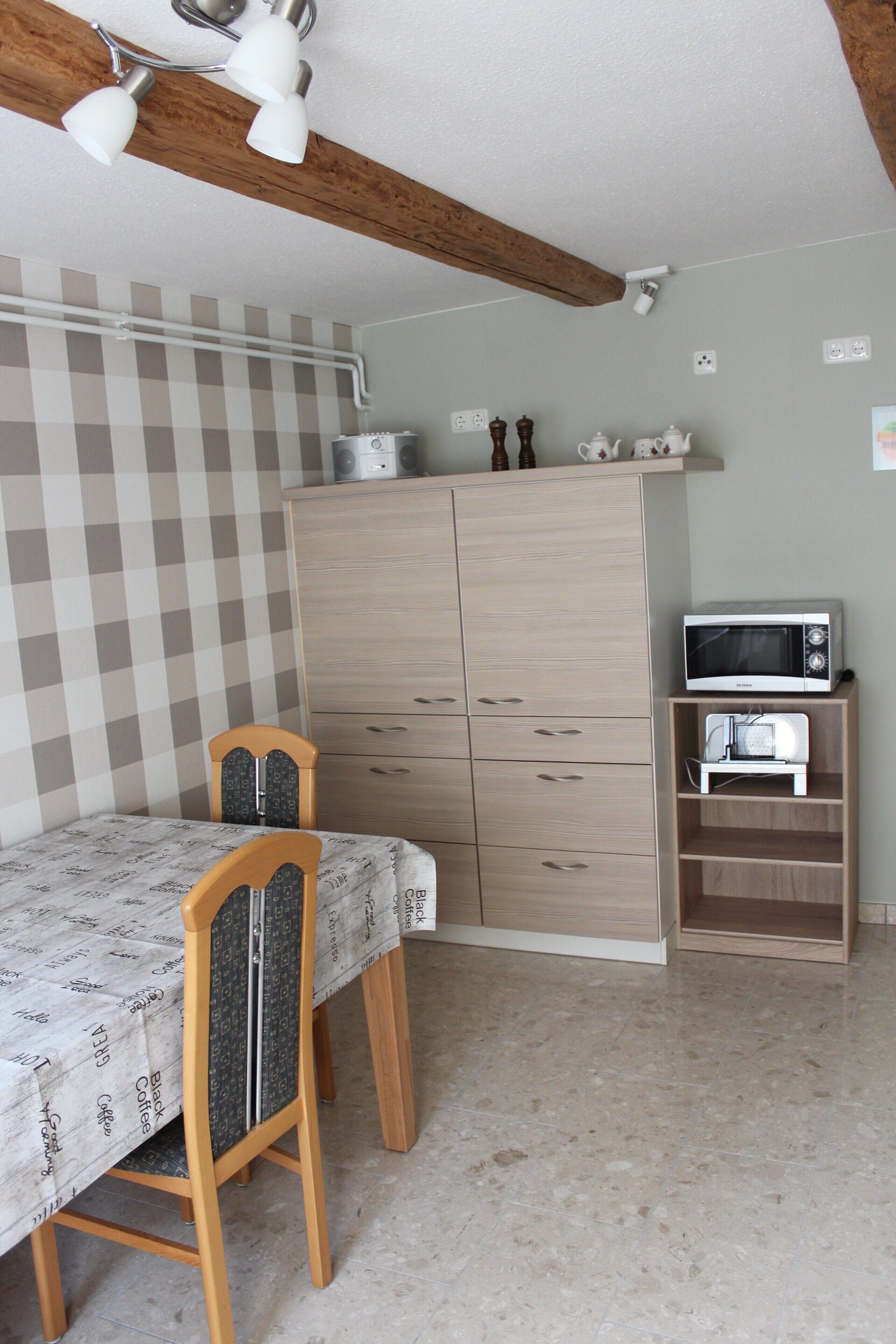 A room with a bed, a wooden chair, a table, a wardrobe, a microwave, and a shelf with a toaster.