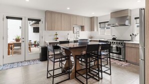 A modern kitchen with a central island, stainless steel appliances, and wooden cabinetry. - Urban Beach House in Downtown Huntington Beach (Huntington Beach)