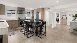 A modern kitchen with a central island, built-in appliances, and a dining area with four chairs. - Urban Beach House in Downtown Huntington Beach (Huntington Beach)