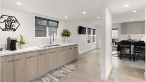 A modern kitchen with a central island, built-in appliances, and a flat-screen TV mounted above the island. - Urban Beach House in Downtown Huntington Beach (Huntington Beach)