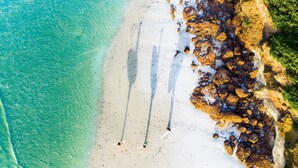 Vista aèria d'una platja amb aigua turquesa cristal·lina, sorra blanca i roques.