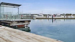 Un port esportiu amb embarcacions amarrades, un edifici amb parets de vidre i un moll de fusta.