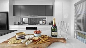A modern kitchen with a wooden cutting board holding snacks and a bottle of champagne. - Village Seaside Retreat - Modern, Walk to Beach (Shellharbour)