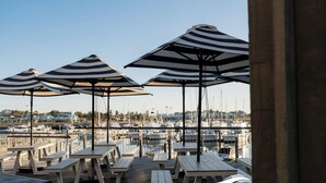 Outdoor seating with striped umbrellas overlooking a marina with boats. - Village Seaside Retreat - Modern, Walk to Beach (Shellharbour)