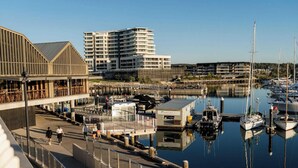 A marina with boats docked, a waterfront promenade, and modern buildings in the background. - Village Seaside Retreat - Modern, Walk to Beach (Shellharbour)