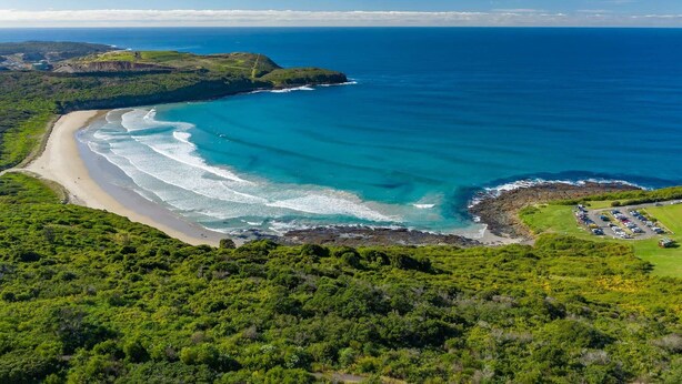 An aerial view of a coastal area with a beach, clear blue waters, and a parking lot. - Village Seaside Retreat - Modern, Walk to Beach (Shellharbour)