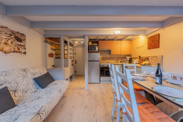 Une cuisine compacte dotée d’appareils électroménagers modernes, un coin repas avec une table dressée pour deux personnes et un coin salon confortable avec un canapé.