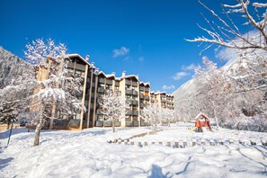 A multi-story building with balconies, surrounded by snow-covered trees and a playground.