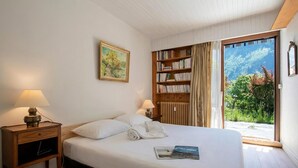 Un letto rifatto con cuscini, un comodino con una lampada, una libreria e vista sul verde attraverso una porta scorrevole.