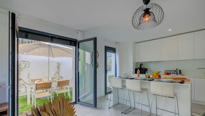 A modern kitchen with white cabinets, a bar area, and a sliding glass door leading to an outdoor dining area. - Apt 2 bedroom - Terrace Near Saint-Tropez, St. Maxime, France (St. Maxime)