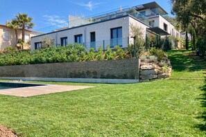 A modern house with a swimming pool, a stone retaining wall, and a well-maintained lawn.