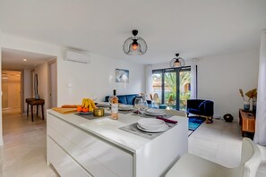 A modern kitchen with white cabinetry, a central island, and a dining area with a blue sofa and a television.