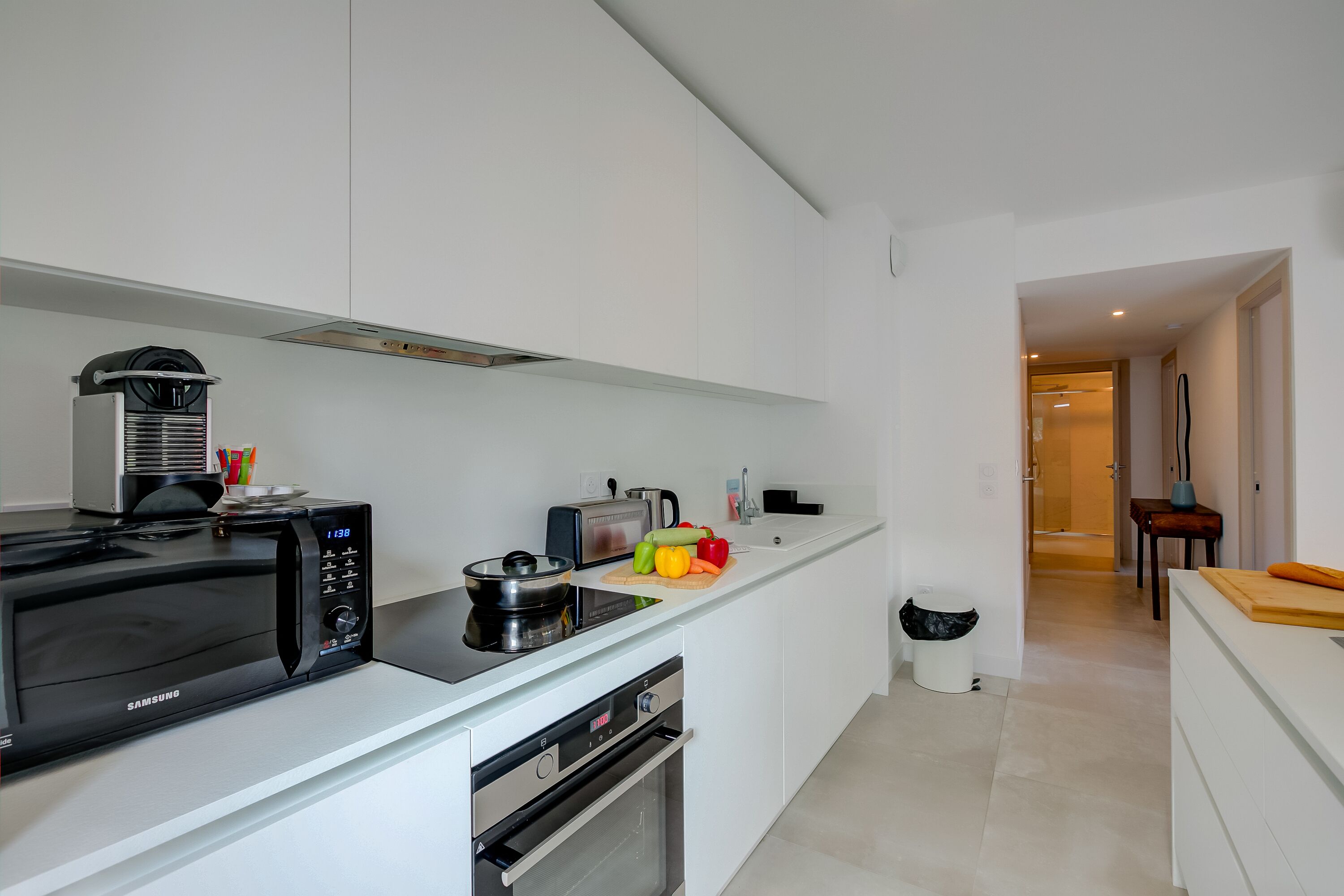 A modern kitchen with a microwave, toaster, and oven. There is a cutting board with vegetables and a sink with a faucet.