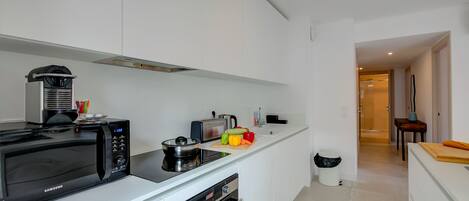 A modern kitchen with a microwave, toaster, and oven. There is a cutting board with vegetables and a sink with a faucet.