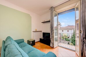 A living room with a sofa, a TV, a small table, and a sliding glass door to a balcony.