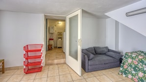 Une pièce avec un canapé gris, une couvre-lit à motifs floraux verts et un panier rouge rempli d’objets.