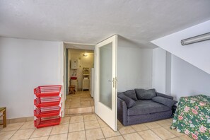 Ein Zimmer mit einem grauen Sofa, einer grün gemusterten Tagesdecke und einem roten Korb mit Gegenständen.