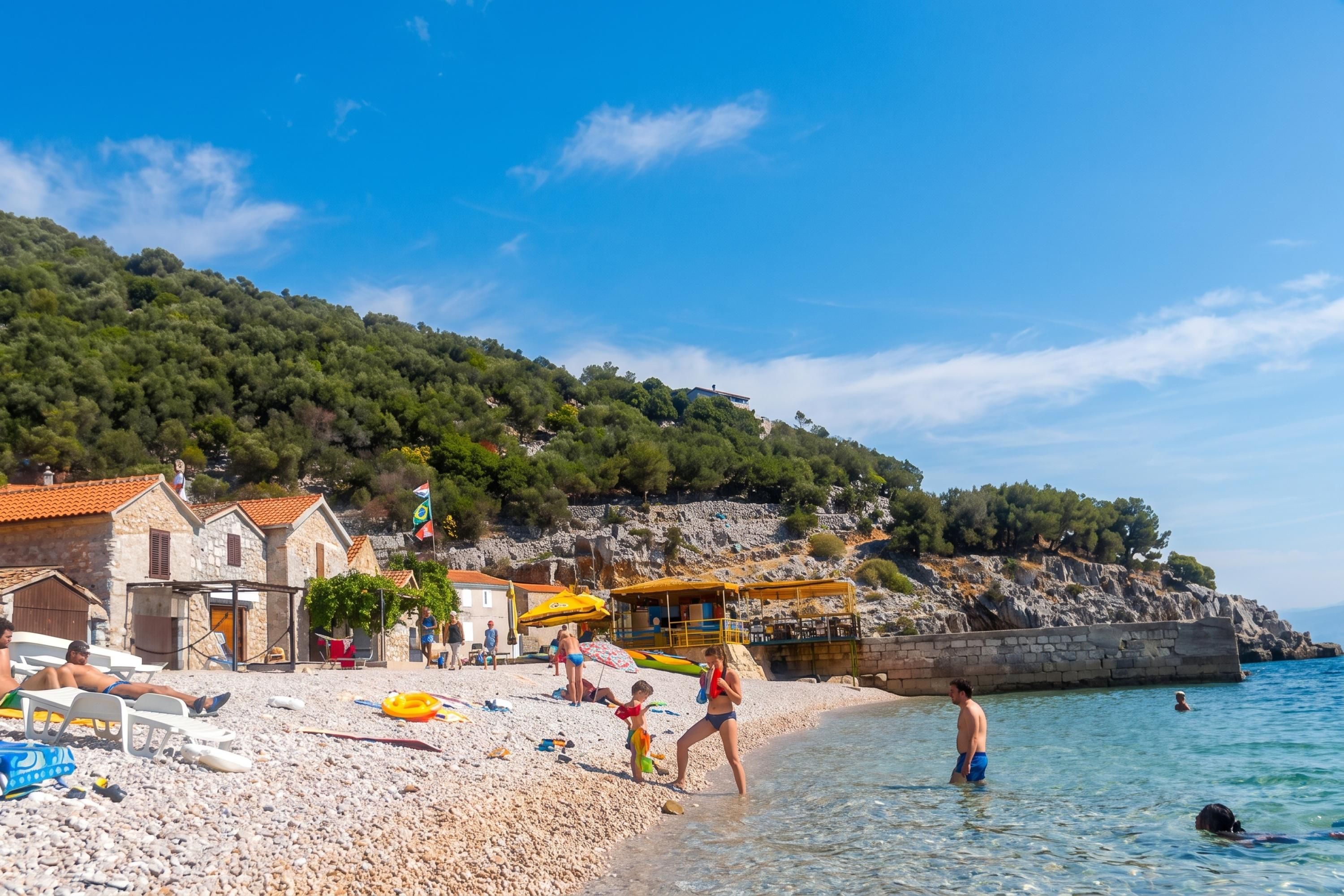 Une plage de galets, quelques personnes et des bâtiments en arrière-plan.