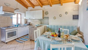 Une cuisine avec des meubles blancs, un plafond en bois et un coin repas avec une table mise pour deux personnes.