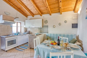 Una cocina con armarios blancos, techo de madera y un comedor con una mesa dispuesta para dos.