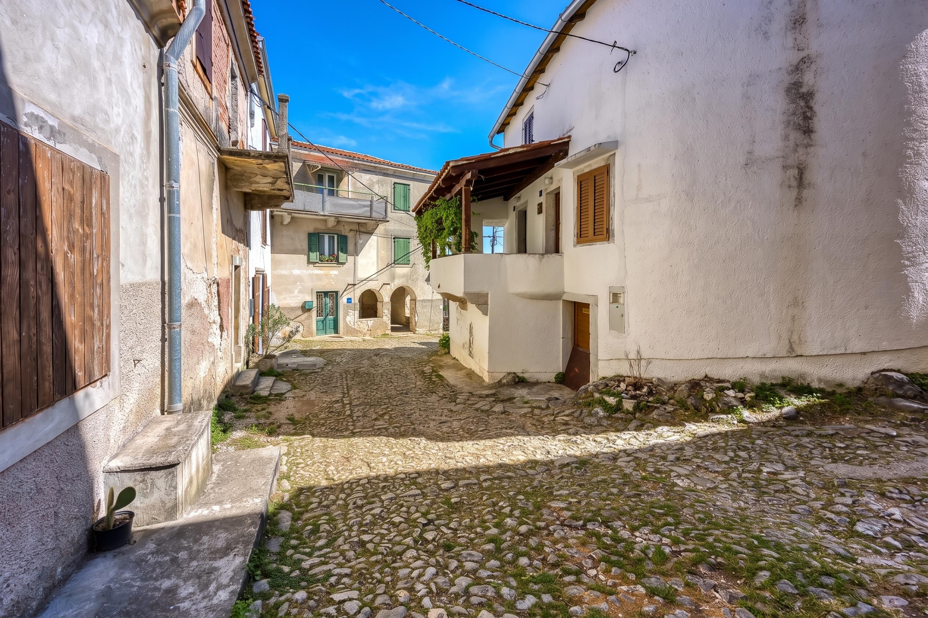 A narrow cobblestone street flanked by buildings with balconies and wooden shutters.