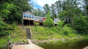 A wooden dock leading to a house with a covered porch and a second house in the background. - Spacious 5 Bedroom Cabin Riverfront/Black Lake Access (Hammond)