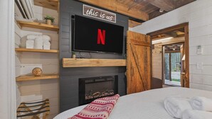 A bedroom with a fireplace, a TV mounted above it, and a bed with a red and white blanket. - Good Times cabin at Saluda Grade Cabins! (Saluda)