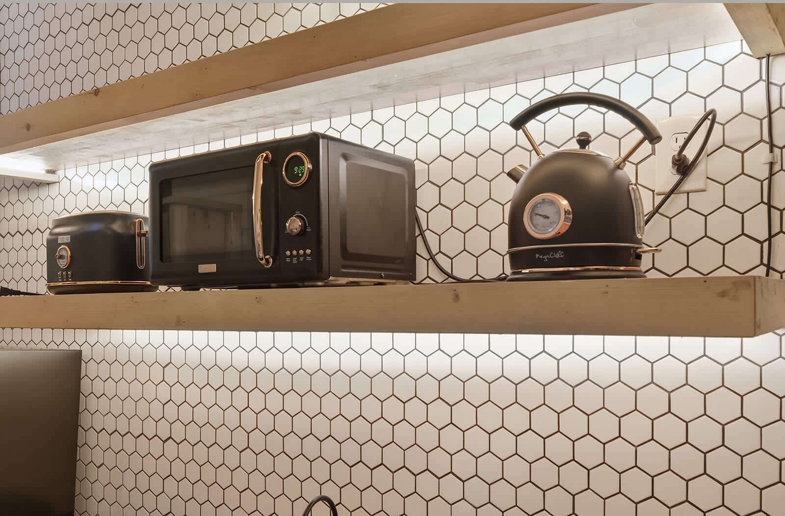 Una cocina con microondas, tostadora y hervidor sobre una repisa frente a un muro de azulejos hexagonales.