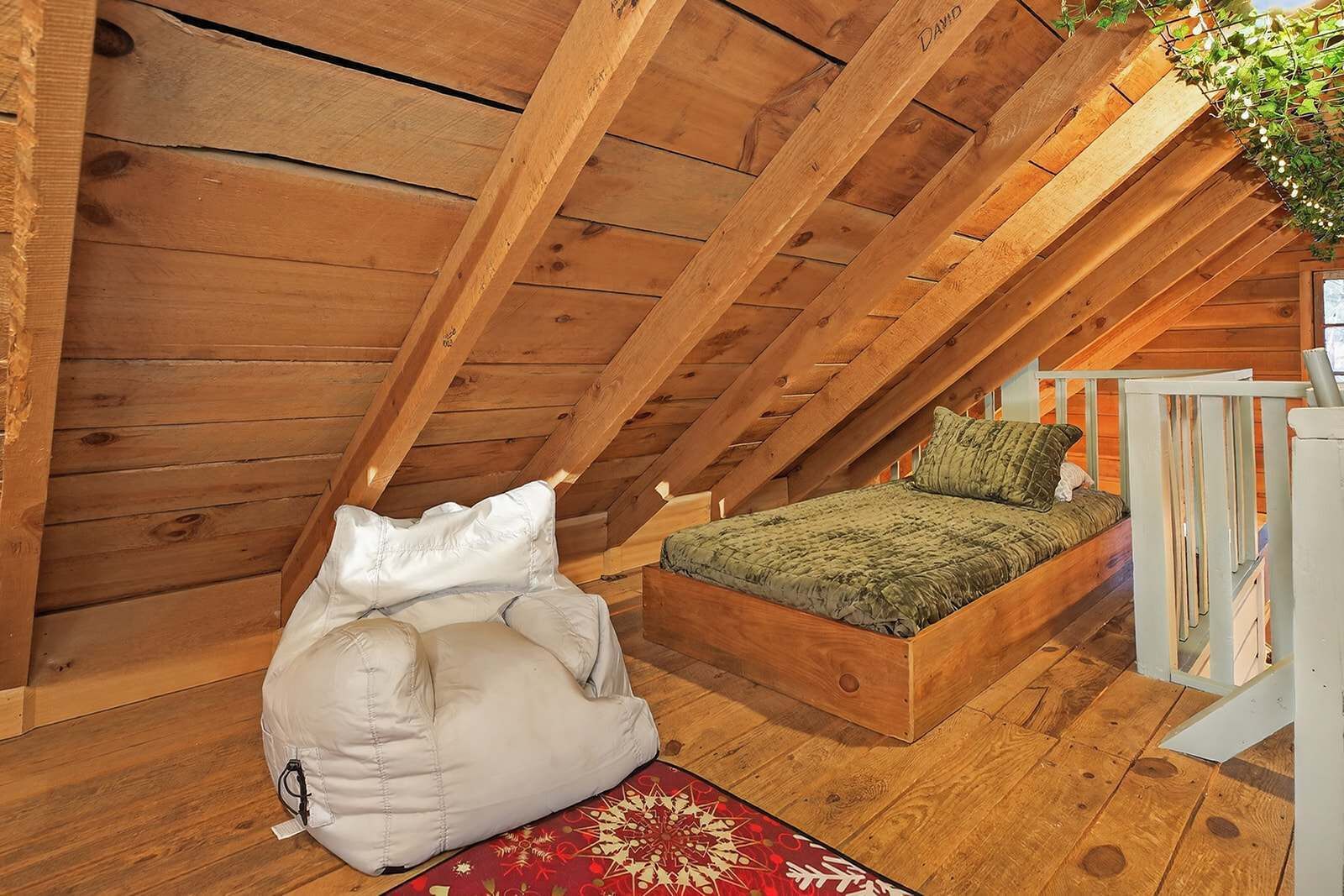 Un dormitorio tipo loft con techo de madera, una cama con ropa de cama verde y una alfombra roja estampada.