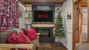 A cozy living room with a fireplace, a Netflix sign, and festive decorations. - Ever After Escape at Saluda Grade Cabins! (Saluda)