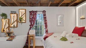 A bedroom with a large bed, a wooden headboard, a window with red and black curtains, a bedside table with a glass of wine, and a plant on the wall. - Ever After Escape at Saluda Grade Cabins! (Saluda)