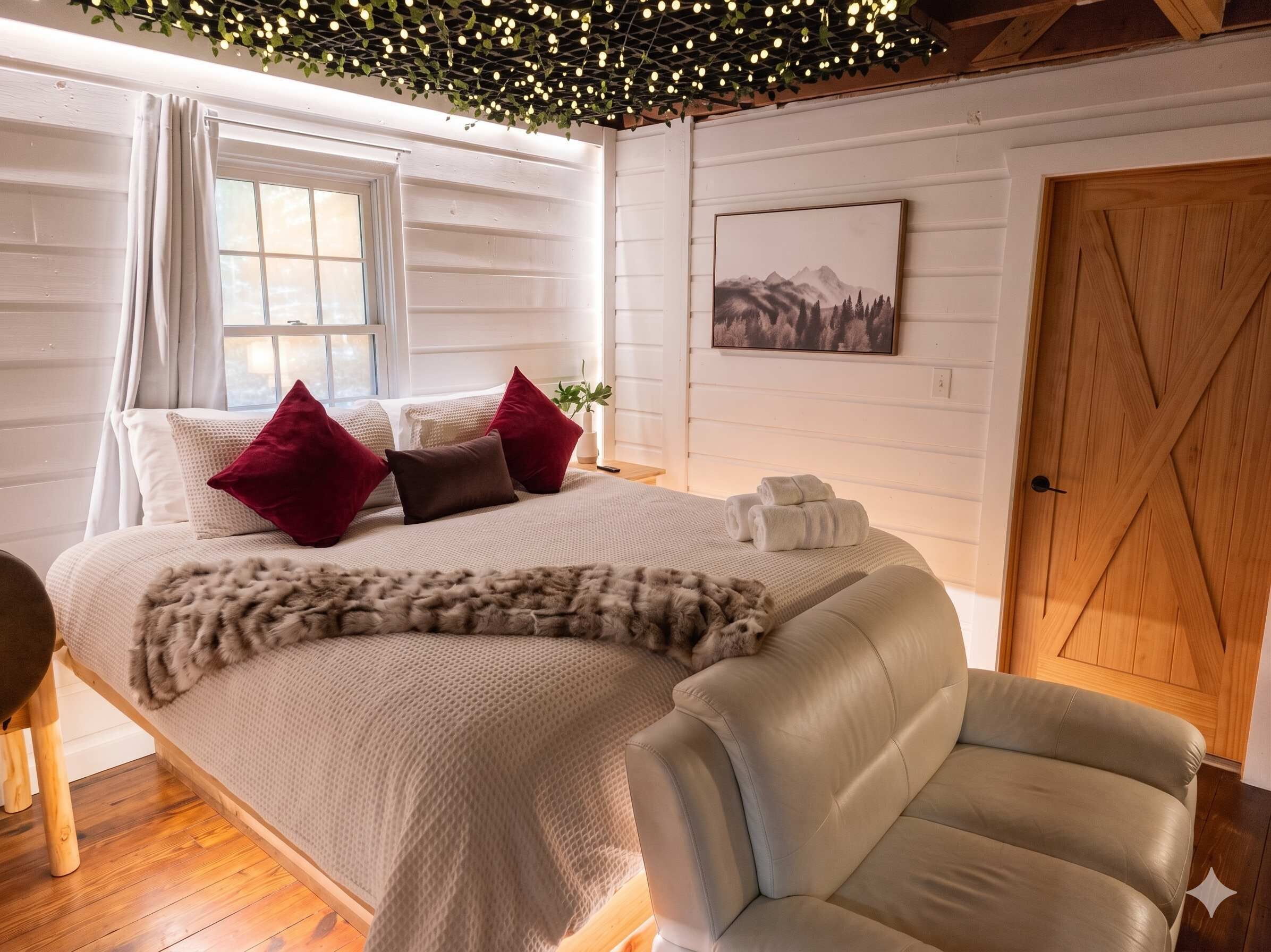 Una camera da letto con un letto, cuscini, una coperta, una sedia, una porta in legno e un quadro appeso al muro.