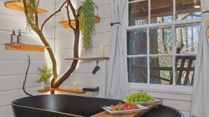 A bathroom with a black bathtub, wooden shelves, a window with a view of trees, and a fruit plate on the side. - Lover's Nest at Saluda Grade Cabins! (Saluda)